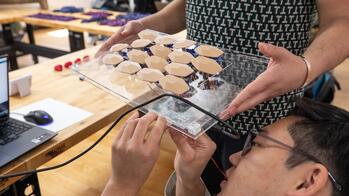 a student attaches wires to a glass device with several nodes, as another student holds the glass attachment surface