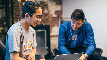 a student works on a laptop as another person observes them working