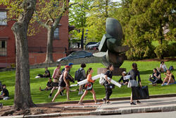 Students carry art supplies and walking past RISD Beach on a beautiful day