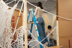 a student stands on a ladder as they and colleagues attach netting to a wood frame