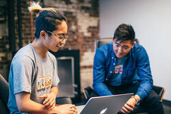a student works on a laptop as another person observes them working