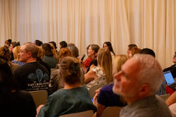 a seated auditorium audience member speaks while holding a microphone
